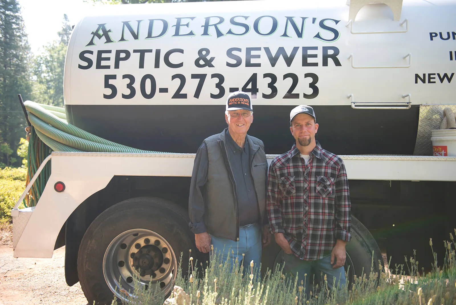 Two Anderson family members standing in front of the Anderson’s Septic & Sewer pump truck