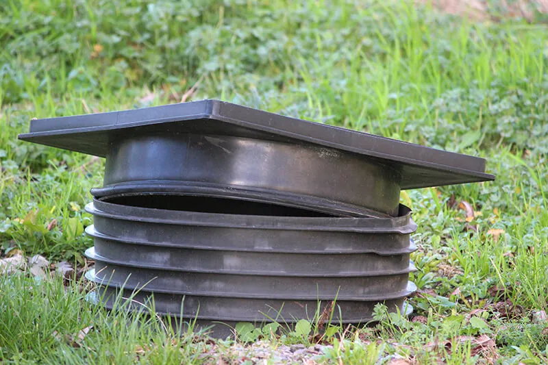 A black plastic septic riser with its lid, sitting in the grass