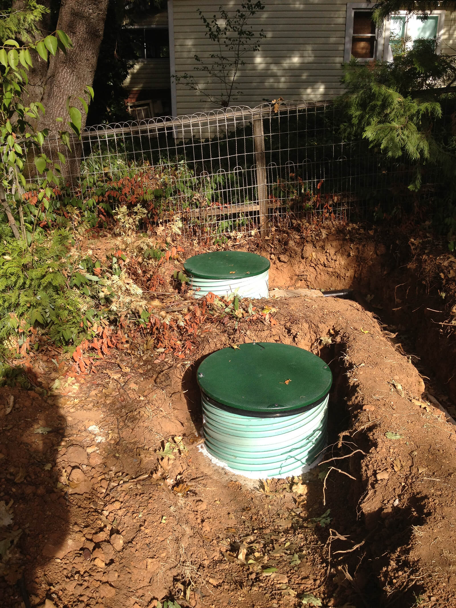 Two green septic tank risers in a freshly dug yard